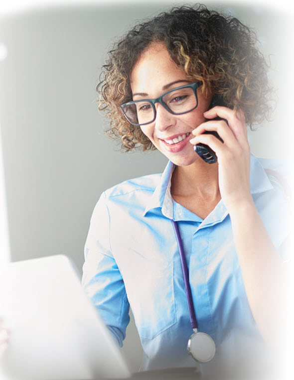 image of a smiling nurse with glasses talking on the phone with stethoscope looking at a laptop and talking on the phone